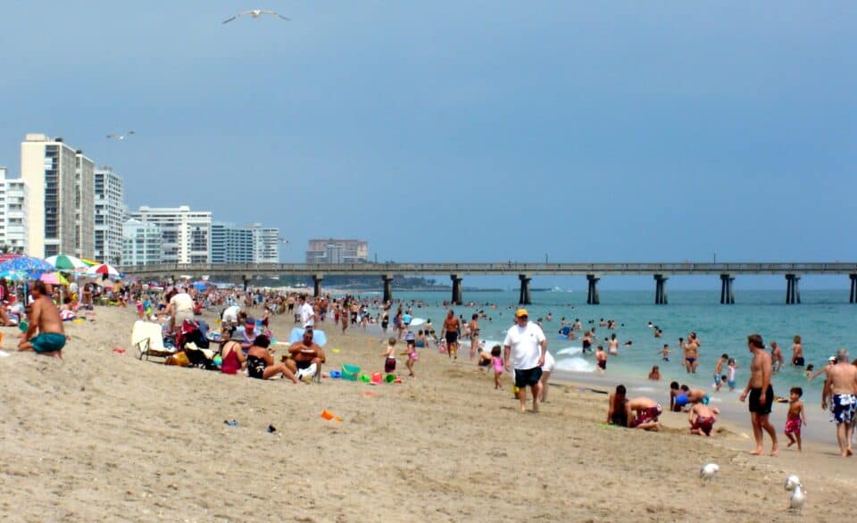 Beachgoers on the sand beside the Deerfield Beach International Fishing Pier in Deerfield Beach, Florida