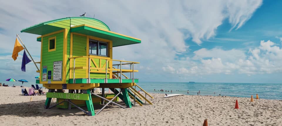 A green and yellow lifeguard tower on the white sand of Miami Beach, Florida