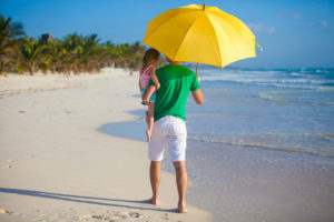 Father holding a yellow umbrella over his child on a Florida beach